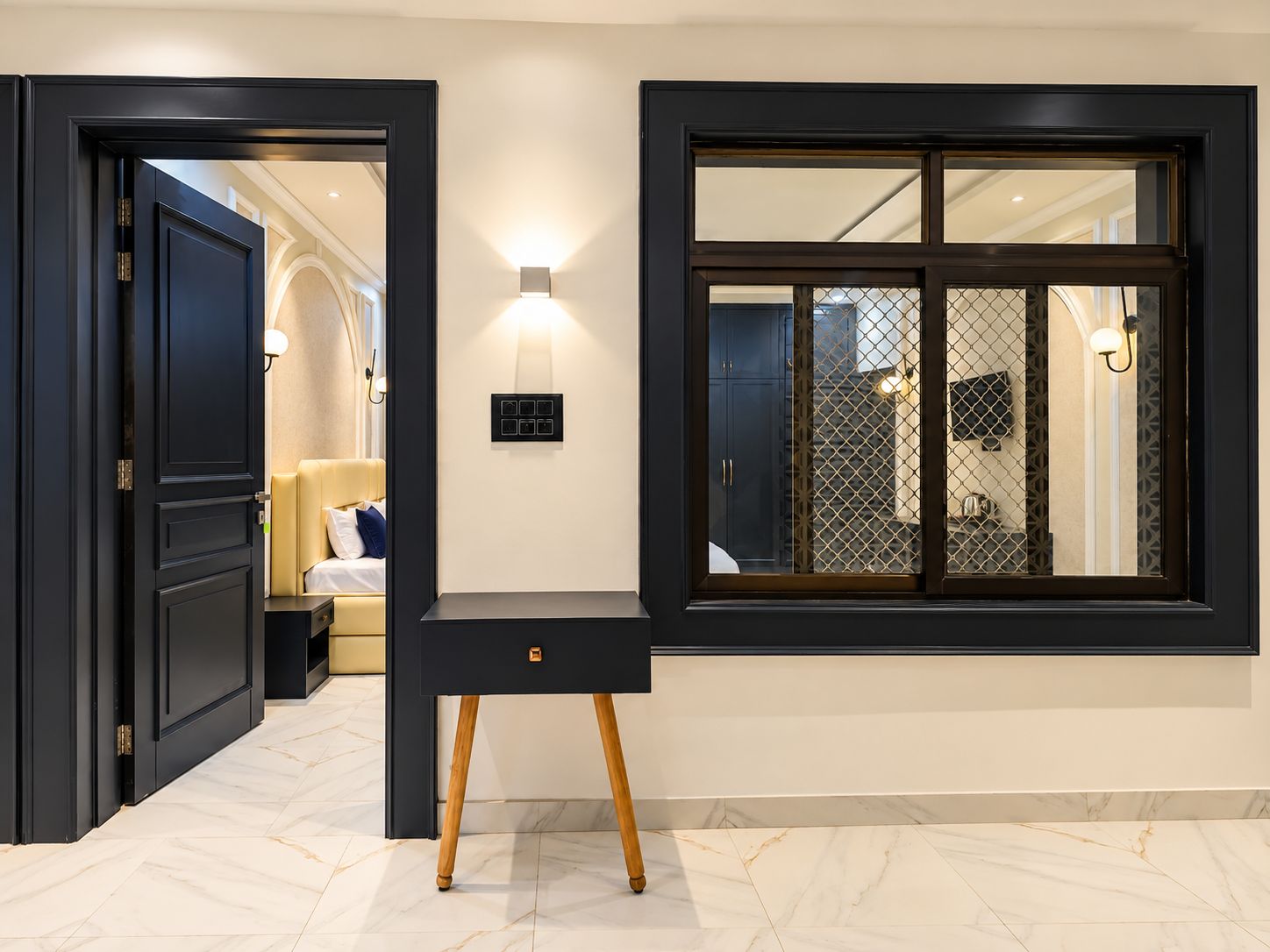A modern interior with a dark wooden door, a black console table with a drawer, and a large window with a decorative grid pattern.