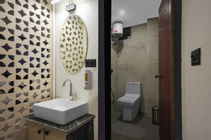 A bathroom with a white sink, a toilet, a shower, and a decorative wall panel. - The Forest Hills Resort (Sarada)