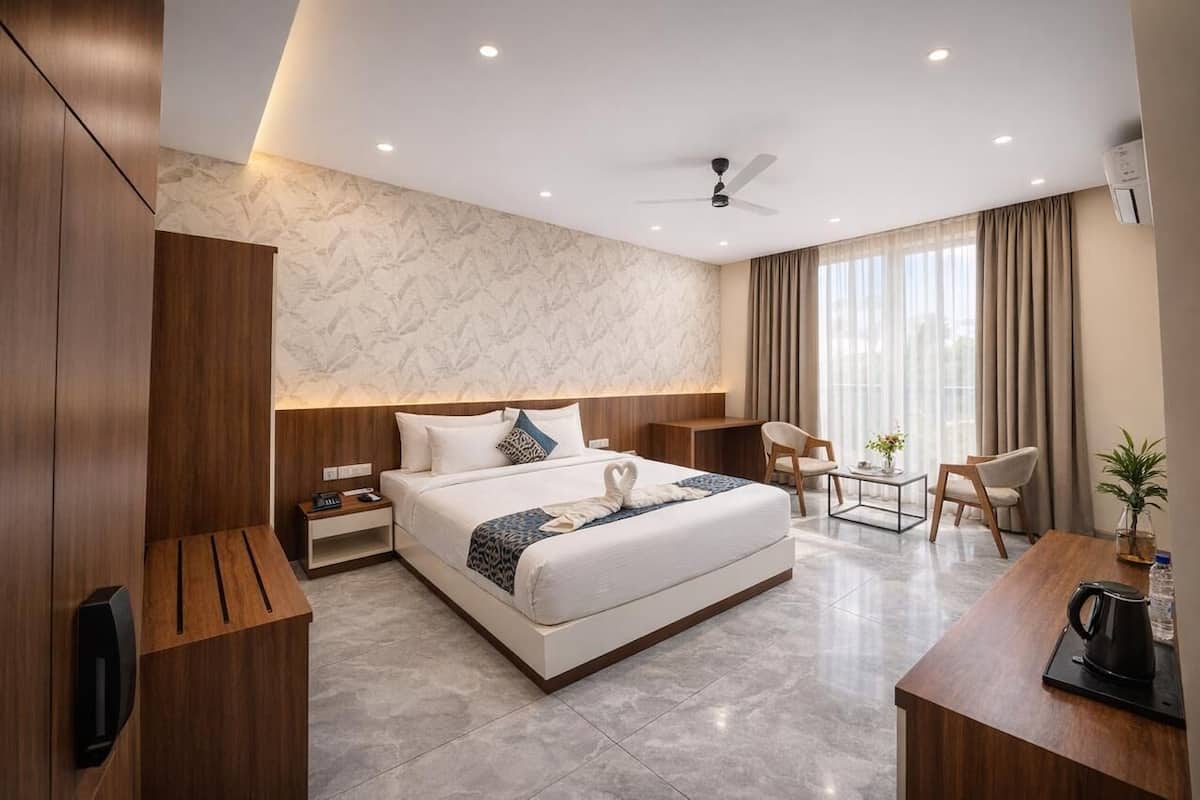 Camera d'albergo con un letto grande, una scrivania, una sedia, un tavolino, una ventola a soffitto e una finestra con tende.