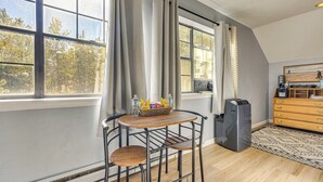 A modern kitchen with a dining area, large windows, and a view of trees. - Fish, Hike & Explore: Mtn-View Lake George Studio (Lake George)