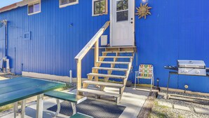 A blue building with a wooden staircase leading to a white door, a picnic table, and a barbecue grill. - Fish, Hike & Explore: Mtn-View Lake George Studio (Lake George)
