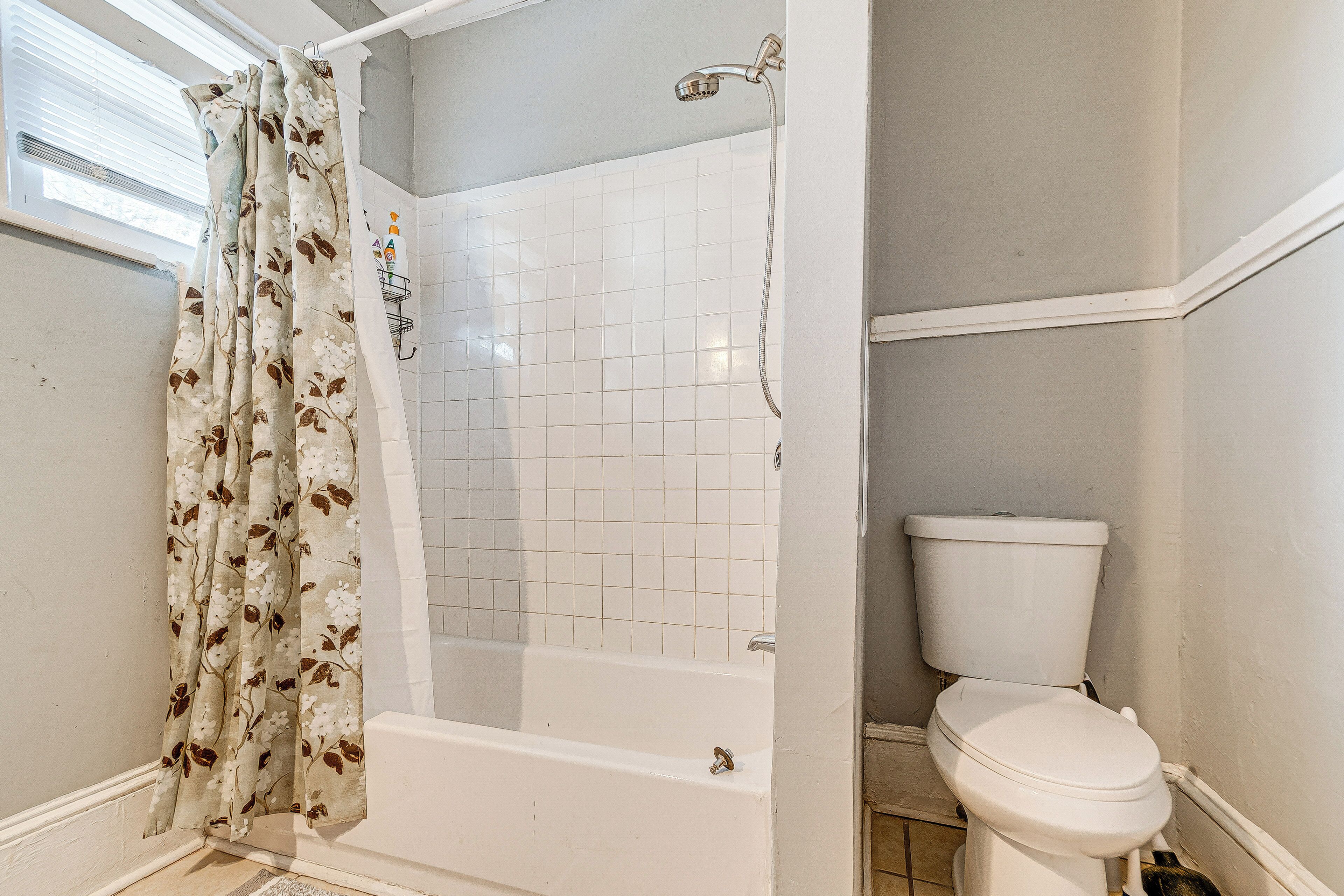 Une salle de bain avec douche, toilettes et une fenêtre équipée de stores.