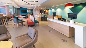 A modern hotel lobby with a reception desk, seating areas, and a large TV screen.
