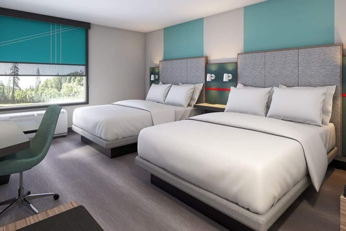 A hotel room with two beds, a desk, a chair, and a window with a view.