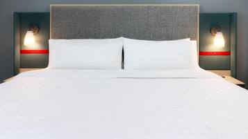 Una cama con cabecera gris, dos mesitas de noche con lámparas y un detalle rojo en las mesitas.