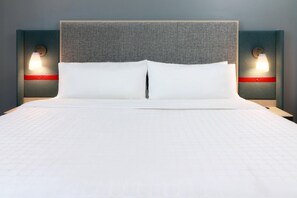 A bed with a grey headboard, two bedside tables with lamps, and a red accent on the tables. - Avid Hotel Fresnillo (Fresnillo)
