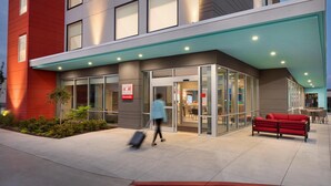 A modern building with a glass entrance, a red wall, and a red bench outside. - Avid Hotel Fresnillo (Fresnillo)