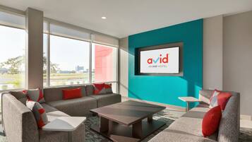 A modern hotel room with a large window, grey sofas, a small table, and a teal accent wall.