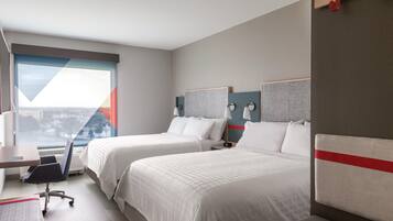A hotel room with two beds, a desk, and a chair. There is a window with a view of the city.