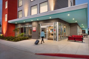 A modern building with a glass entrance, a red wall, and a red bench outside. - Avid Hotel Fresnillo (Fresnillo)