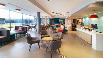 A modern hotel lobby with seating areas, a reception desk, and large windows offering views.