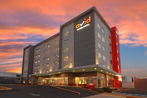 Un moderno edificio de hotel con un llamativo letrero 'Avid', varios pisos y un estacionamiento.