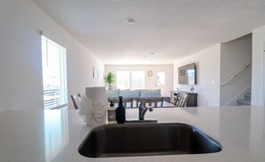A modern kitchen with a stainless steel sink, a dining area with a sofa and chairs, and a staircase leading to another level. - Brand new cozy 4BR home- sleeps up to 10, beach gear, 1gbps WiFi,full kitchen! (Panama City)