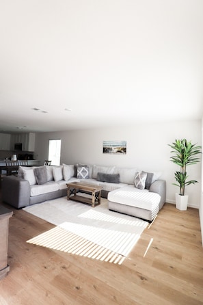 A modern living room with a grey sectional sofa, a wooden coffee table, and a large potted plant. - Brand new cozy 4BR home- sleeps up to 10, beach gear, 1gbps WiFi,full kitchen! (Panama City)
