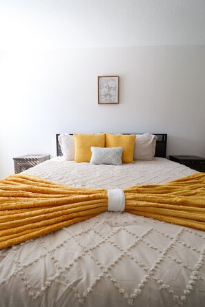 A neatly made bed with a yellow blanket, white quilted bedspread, and multiple pillows in various colors. - Brand new cozy 4BR home- sleeps up to 10, beach gear, 1gbps WiFi,full kitchen! (Panama City)