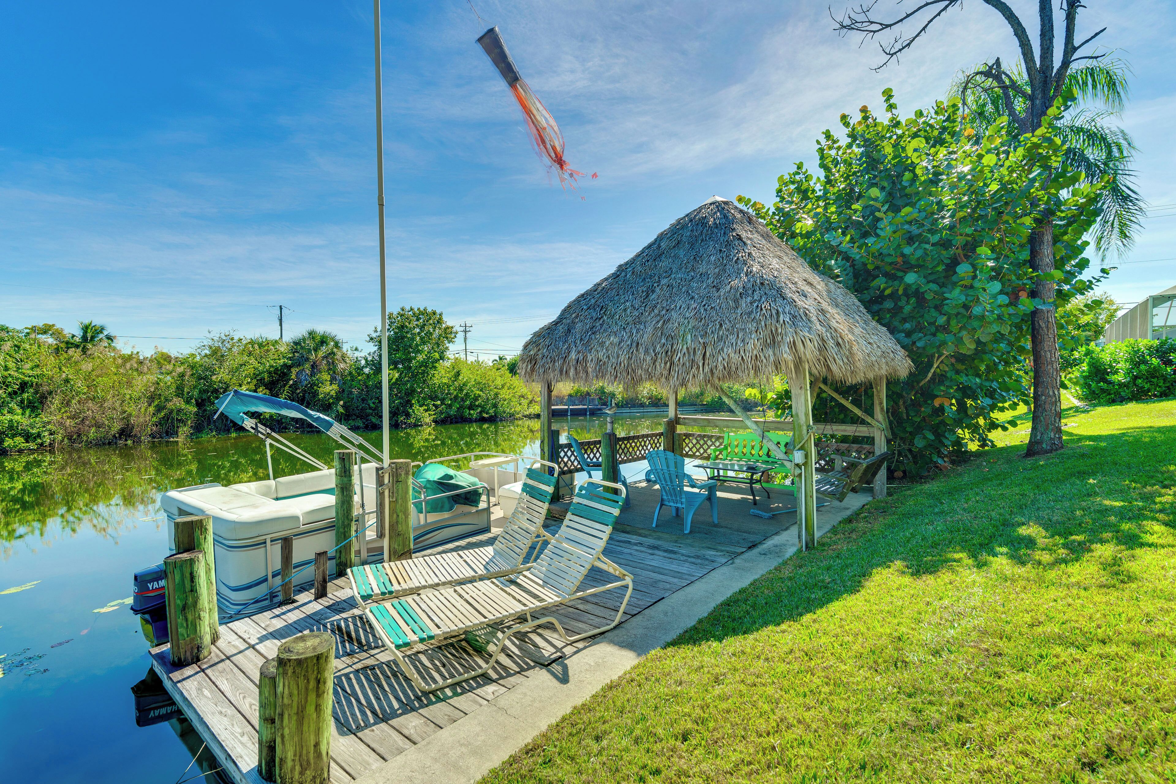 A dock with a thatched-roof structure, lounge chairs, and a boat.