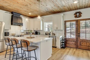A modern kitchen with white cabinets, a large island with bar stools, stainless steel appliances, and a wooden ceiling. - Unplugged Getaway on Lake Secession! Home w/ Dock (Abbeville)