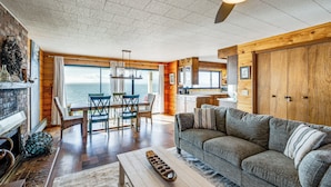 Una sala de estar acogedora con chimenea, una mesa de comedor de madera y un amplio ventanal con vistas al océano.