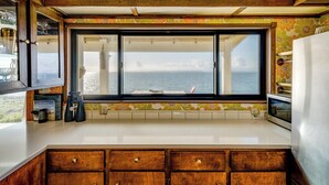 Una cocina con armarios de madera, encimera blanca y un amplio ventanal con vistas al mar.