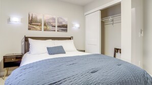 Una cama bien hecha con un edredón azul, dos lámparas de pared y dos cuadros de paisajes encima.