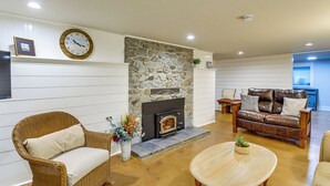 A living room with a stone fireplace, wicker furniture, and a wooden coffee table. - Peaceful Patio View! Waterfront Puget Sound Unit (Poulsbo)