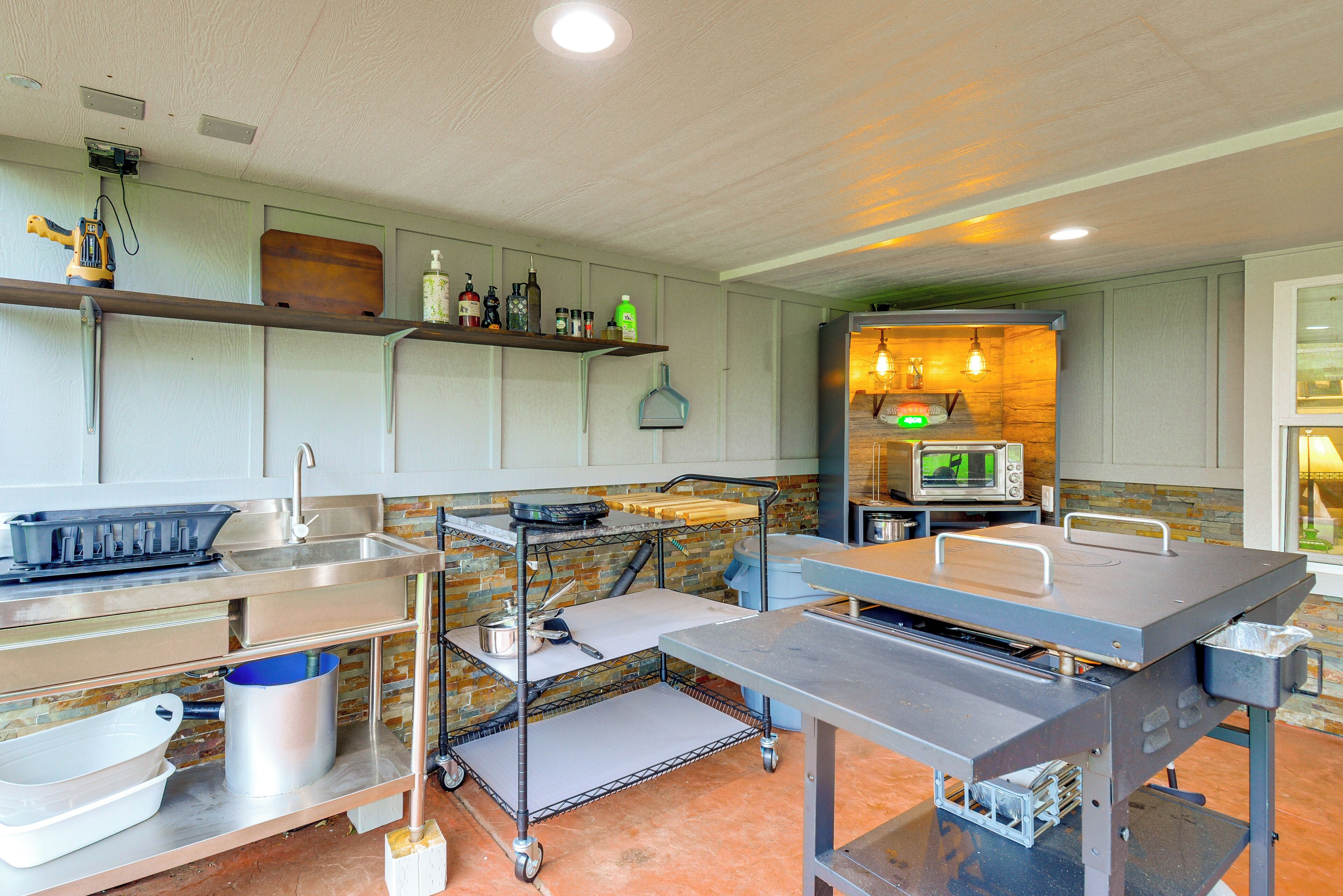 A modern kitchen with stainless steel appliances, a brick backsplash, and a wooden shelf.