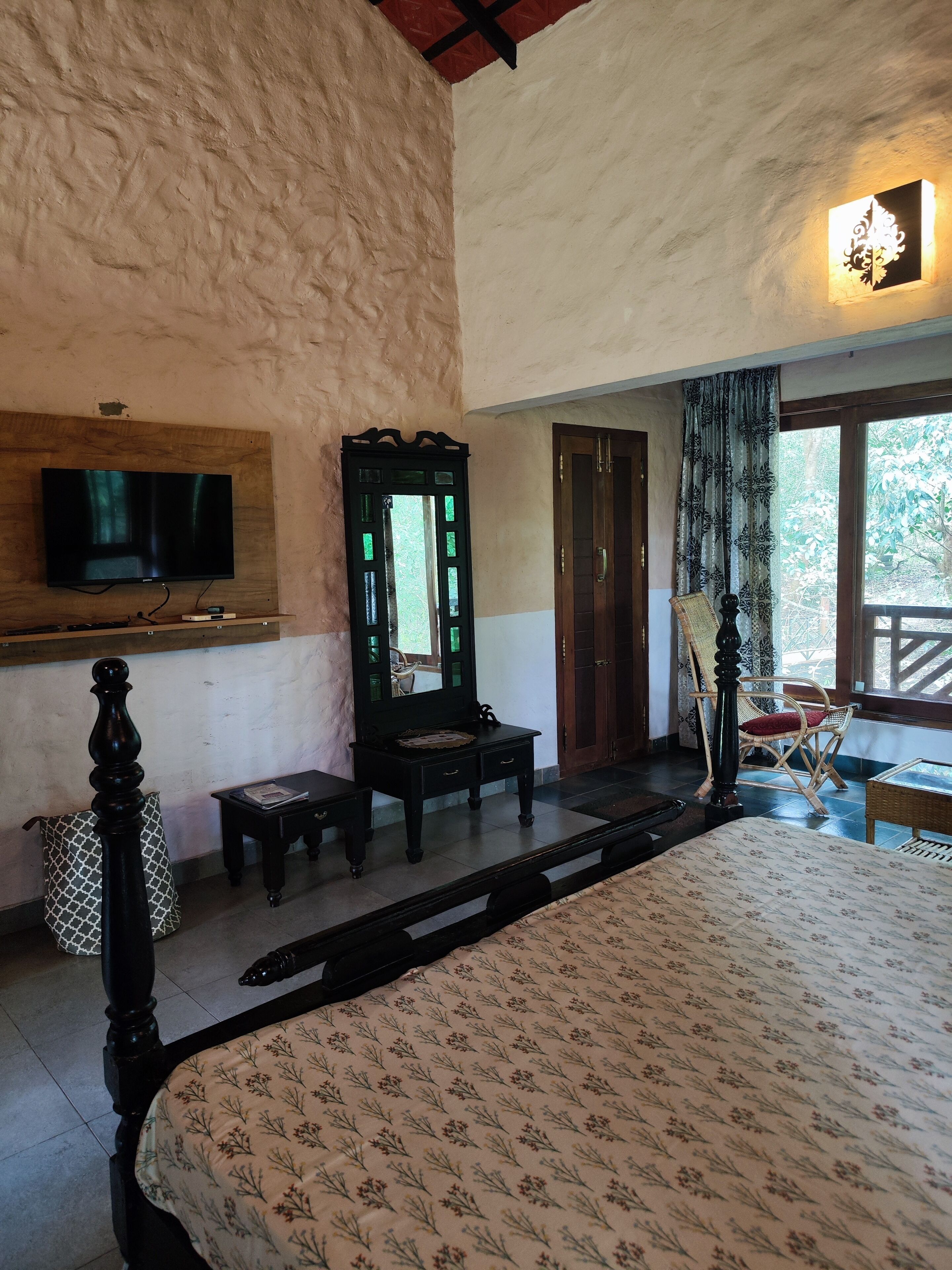 A bedroom with a large bed, a television mounted on the wall, a wooden dresser, and a mirror.