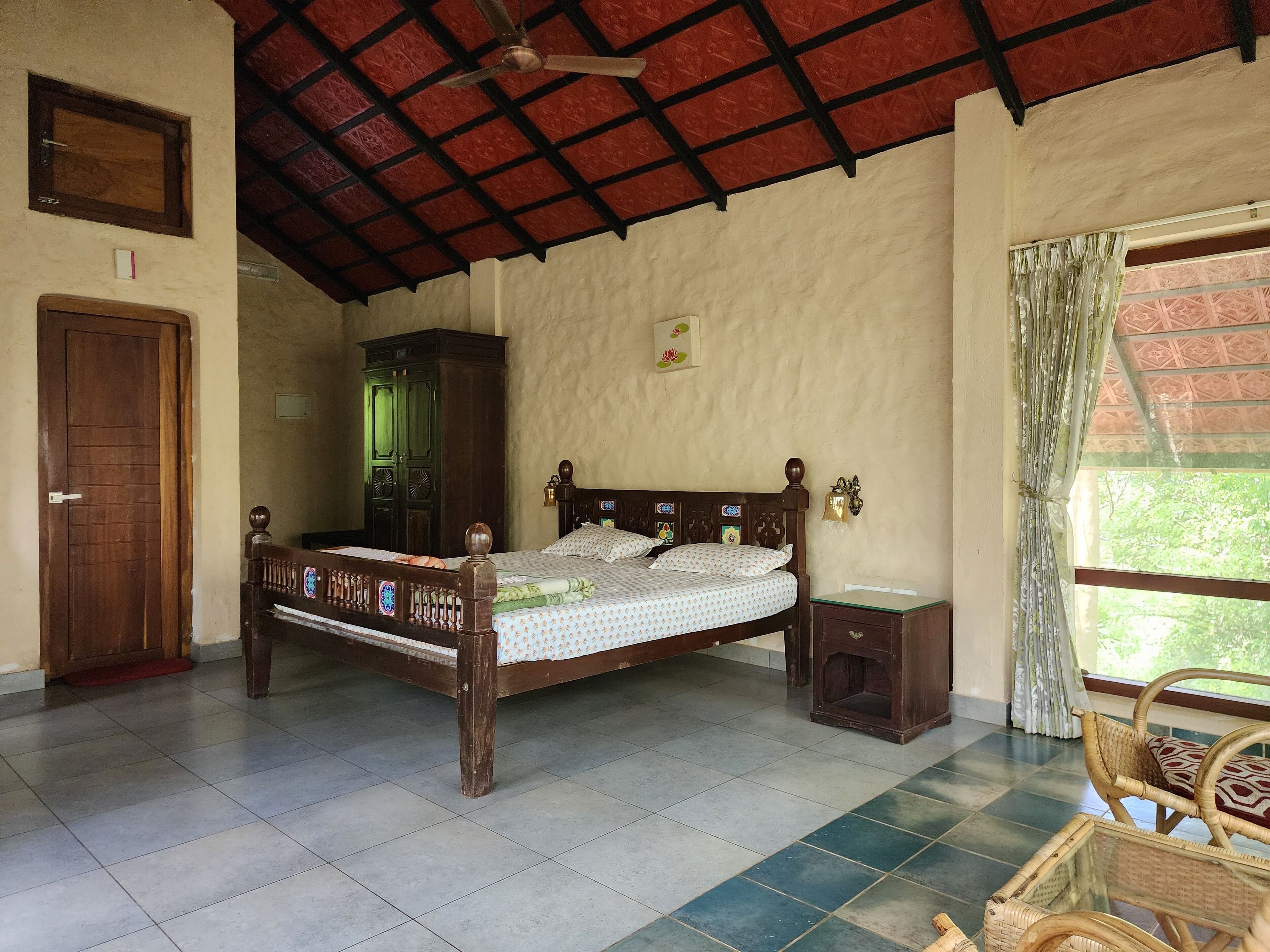 A room with a wooden bed, a wardrobe, a small table, and a window with curtains.
