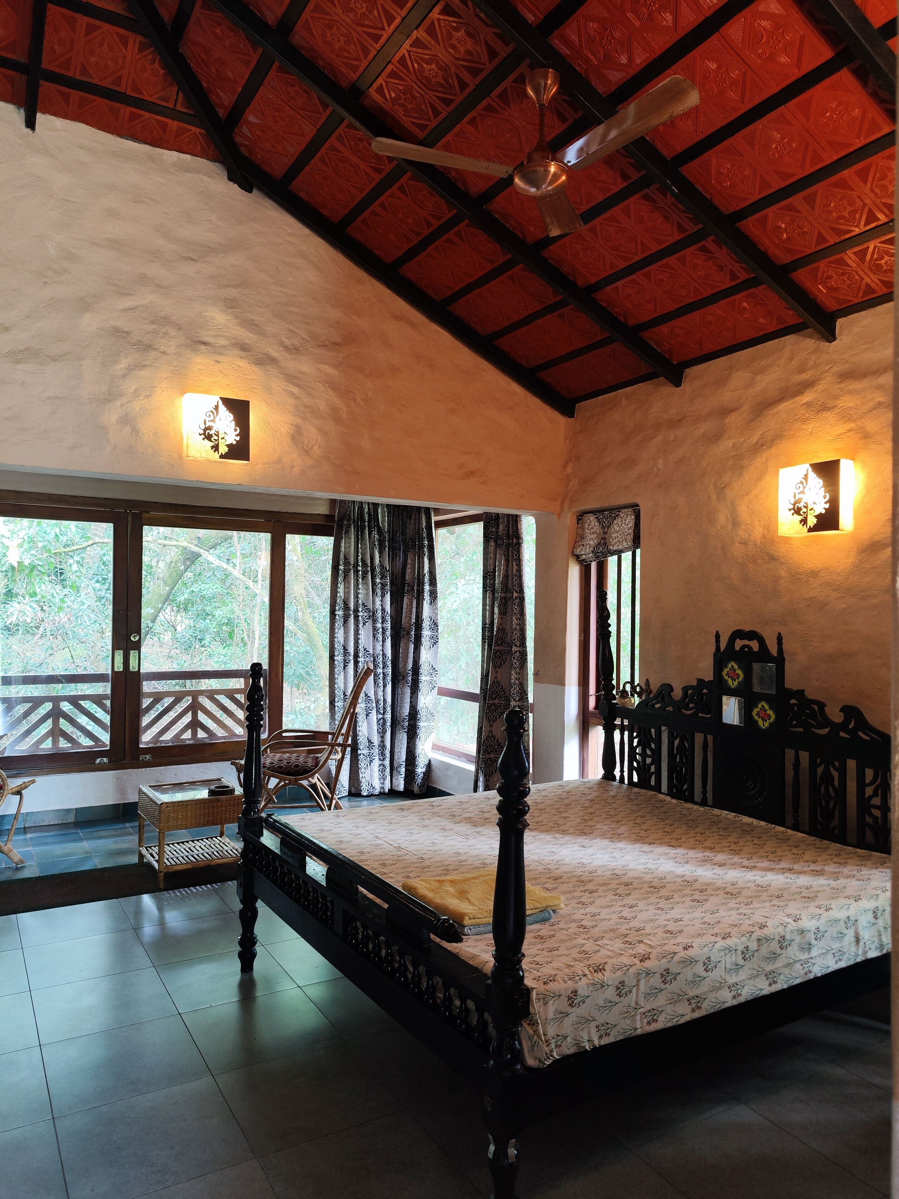 A spacious room with a large bed, a ceiling fan, and a balcony with a view of greenery.