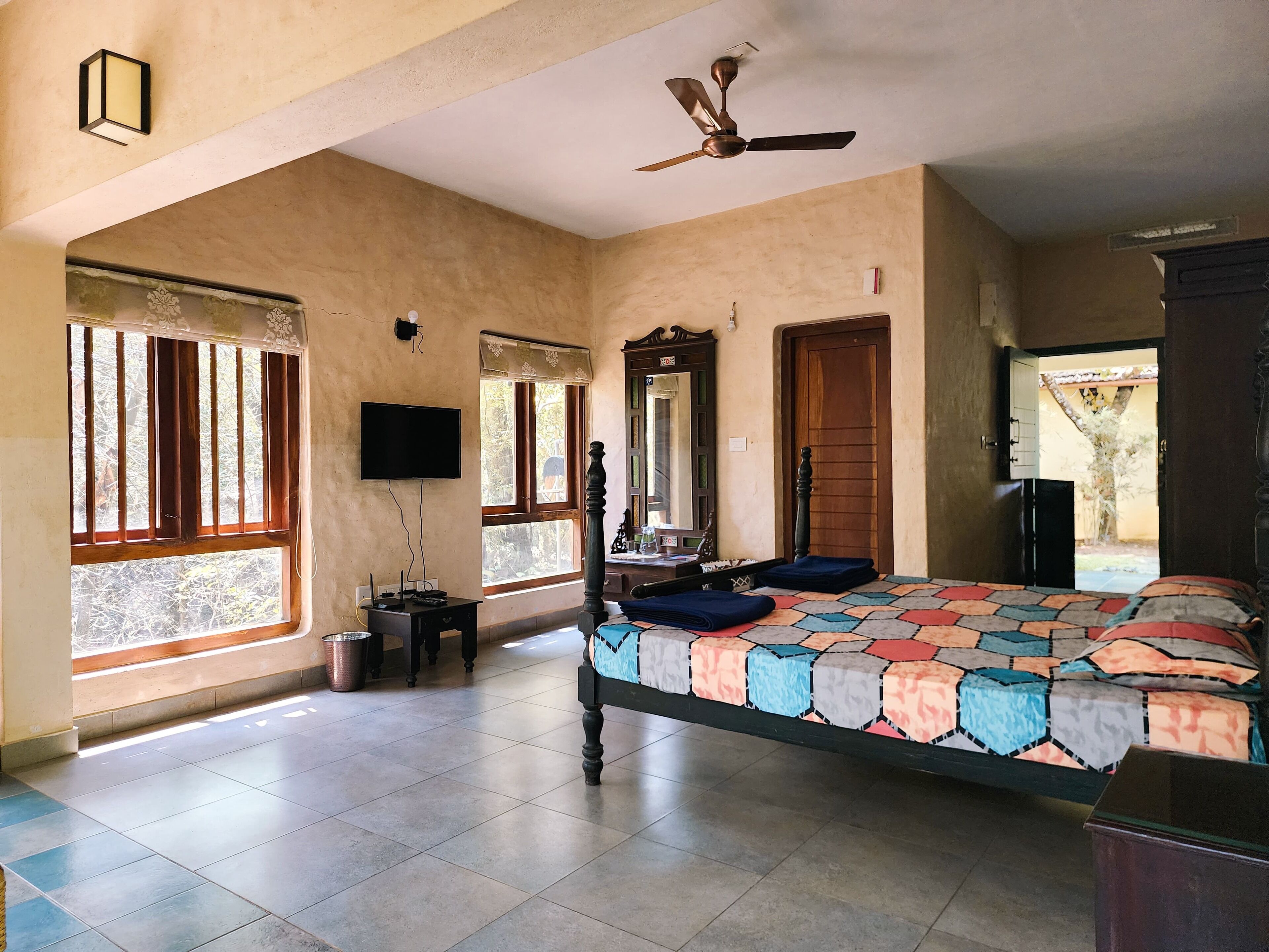 Un dormitorio espacioso con una cama grande, ventilador de techo, televisor y ventana con vista al exterior.