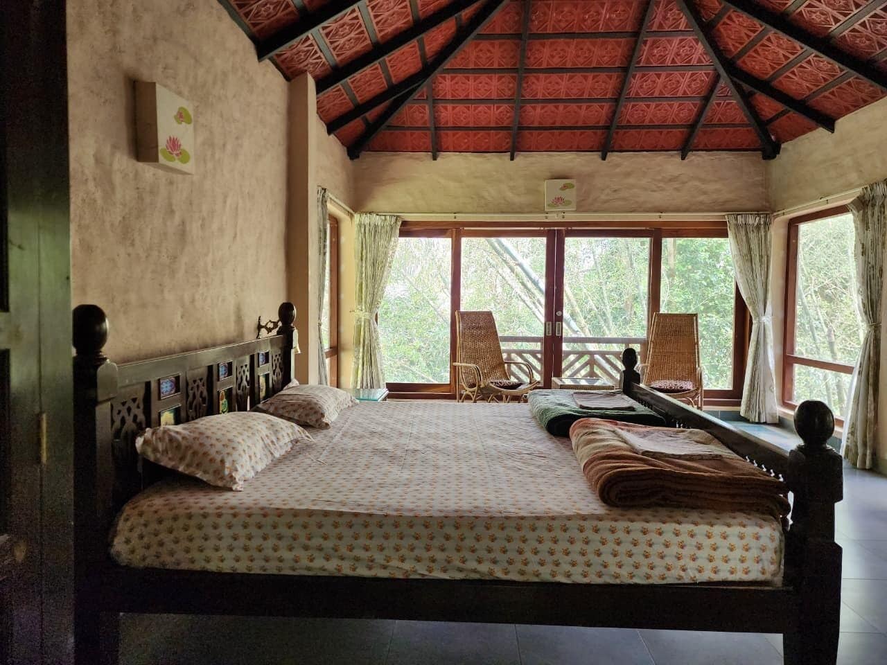 A bedroom with a large bed, wooden headboard, and a view of the outdoors through large windows.