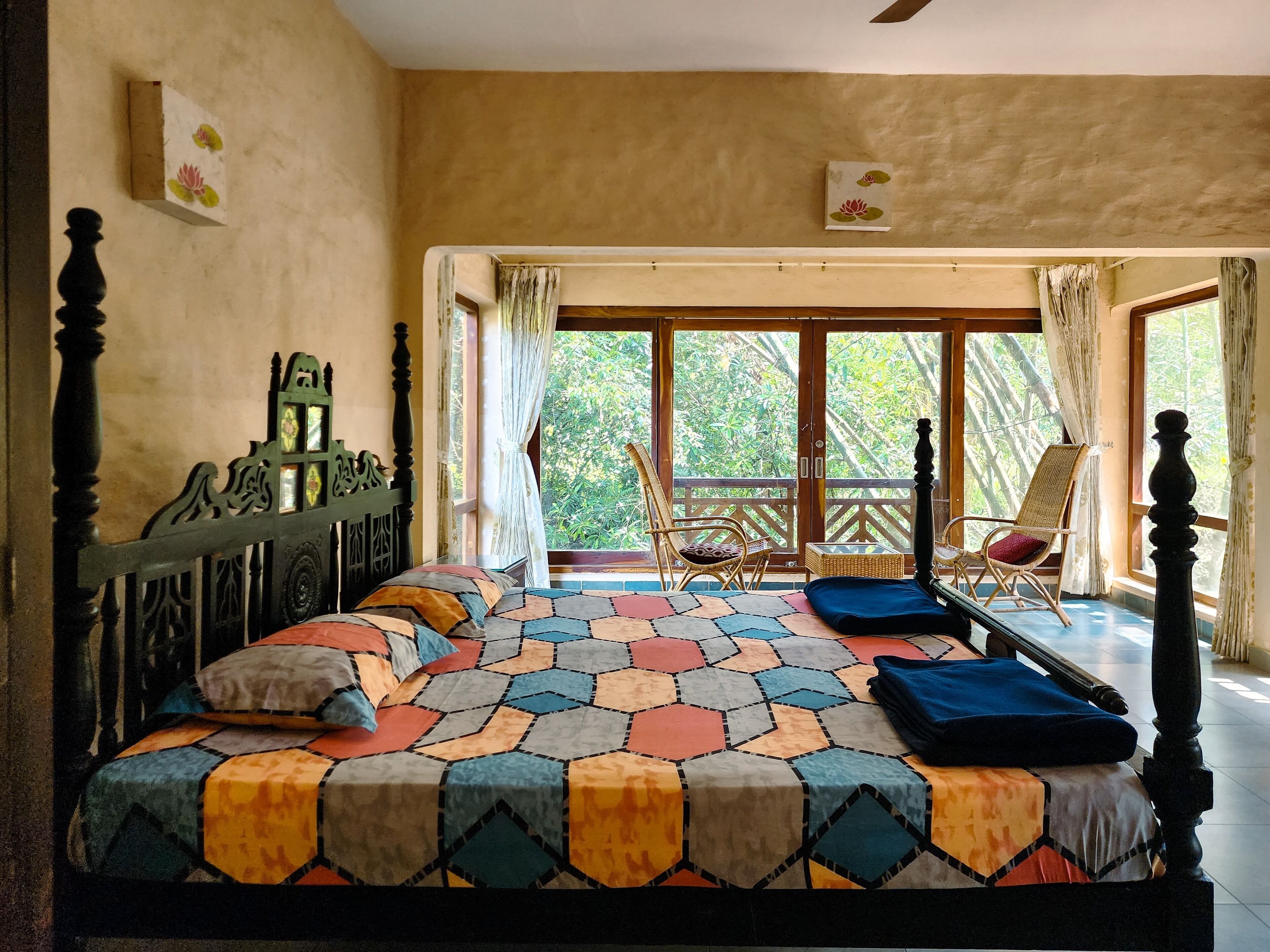 Un dormitorio con cama, cabecera de madera, ventana con cortinas, balcón con una silla y vista a zonas verdes.