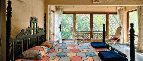 Un dormitorio con cama, cabecera de madera, ventana con cortinas, balcón con una silla y vista a zonas verdes.