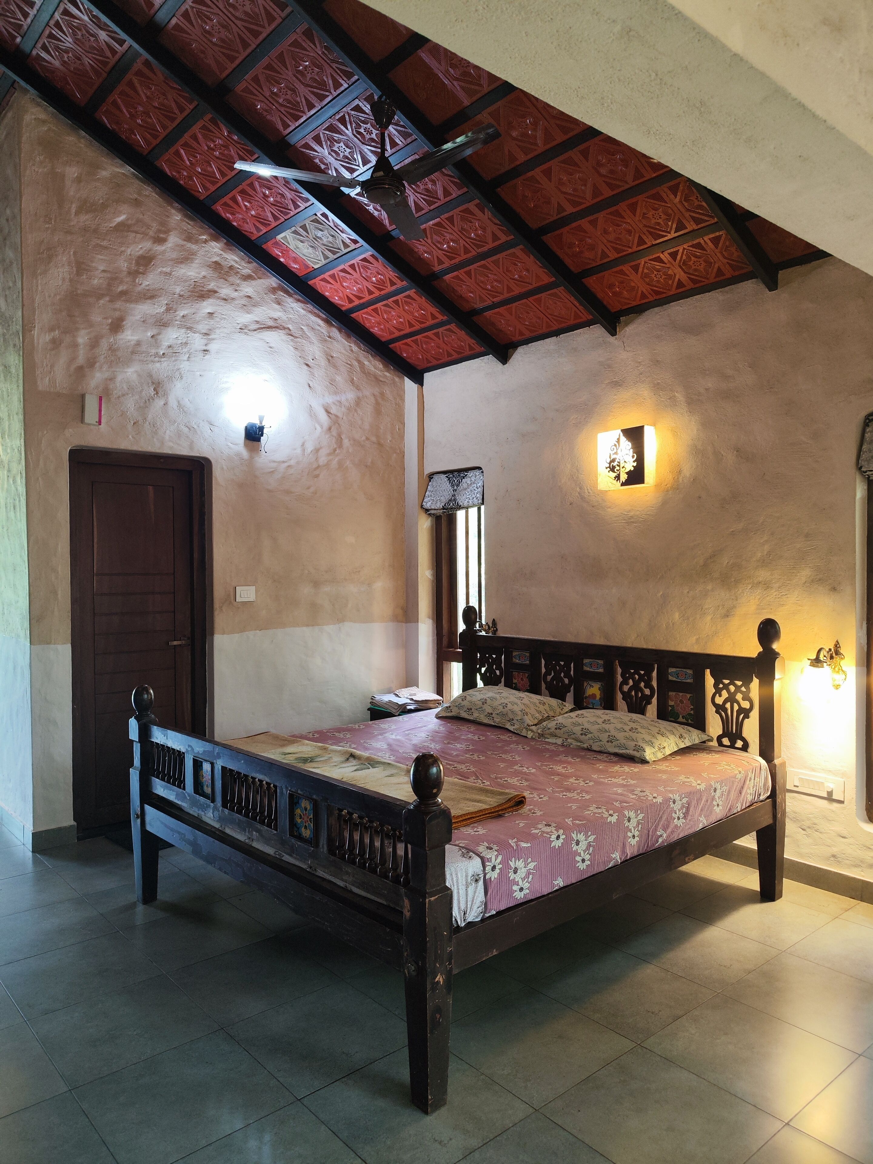 Ein Schlafzimmer mit einem hölzernen Bett, einer Tür, einer Wandleuchte und einem Deckenventilator.