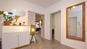 Ein Flur mit einem weißen Schrank, einer Korbpflanze, einer Stehlampe und einem großen Spiegel an der Wand.