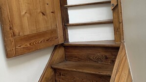 Eine Holztreppe, an einer Seite eine weiße Wand und auf der anderen eine Holztür.