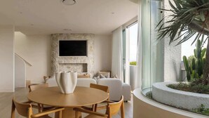 A modern interior with a dining area, a stone fireplace, and a large window with a view of a cactus garden. - Cala by Khove (Burleigh Heads)