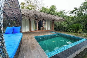 A poolside area with a wooden deck, a blue cushioned seating area, and a thatched-roof structure. - Bellevue Beach Nilaveli BY PARADISE COLLECTION (Nilaveli)