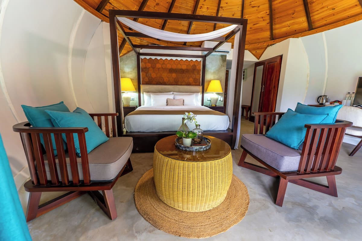 A bedroom with a four-poster bed, two nightstands with lamps, and a round wicker coffee table with a plant.