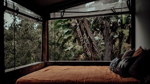 Une chambre avec une grande fenêtre donnant sur un feuillage dense.