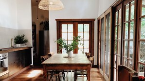 Une cuisine spacieuse avec une table et des chaises en bois, un luminaire suspendu et de grandes fenêtres donnant sur un paysage verdoyant.