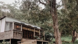 Un chalet rustique avec des fondations en pierre, une terrasse en bois et de grandes fenêtres.