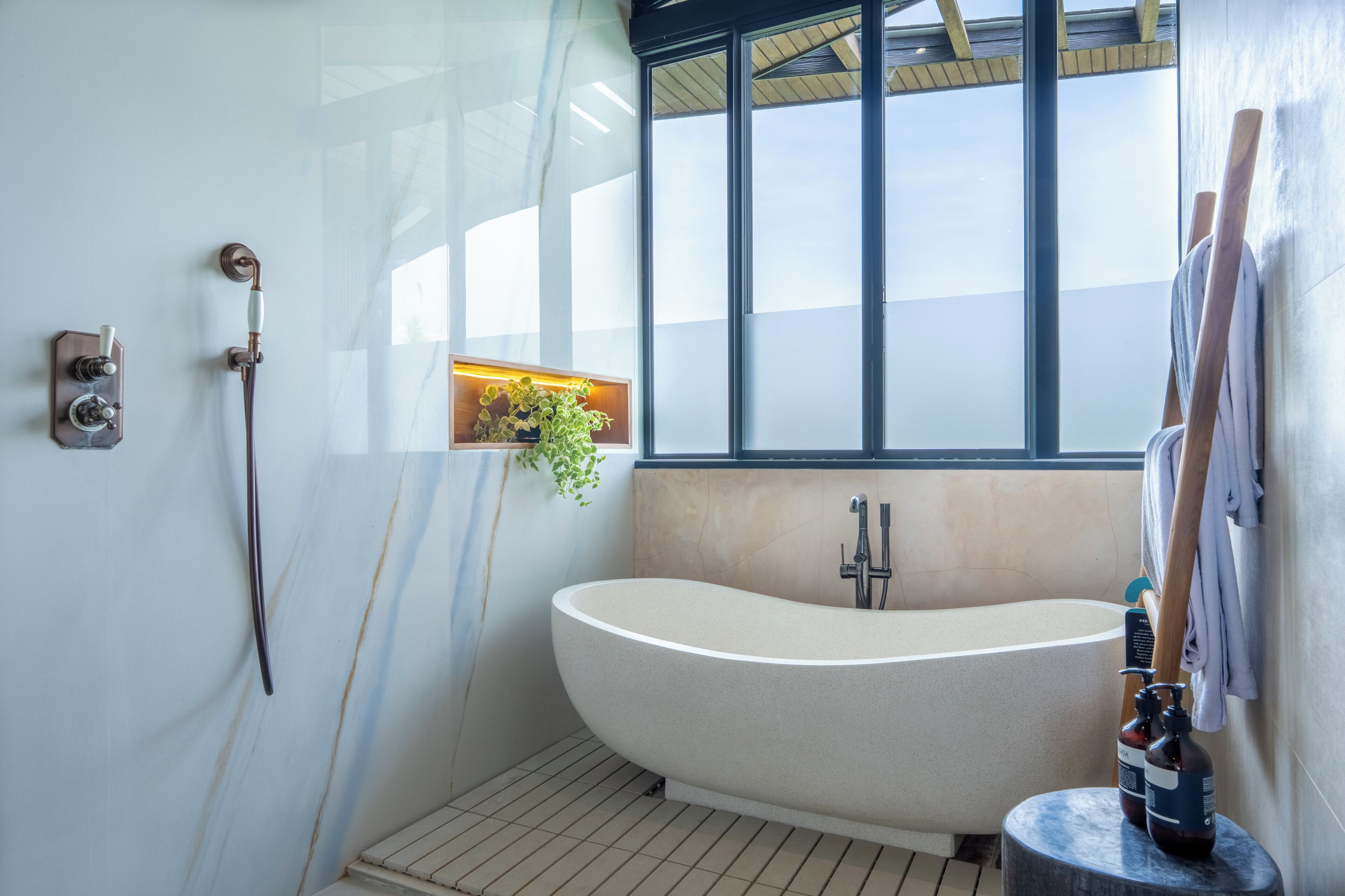 Een moderne badkamer met een vrijstaand bad, een douchekop, een handdoekhouder en een raam met uitzicht.