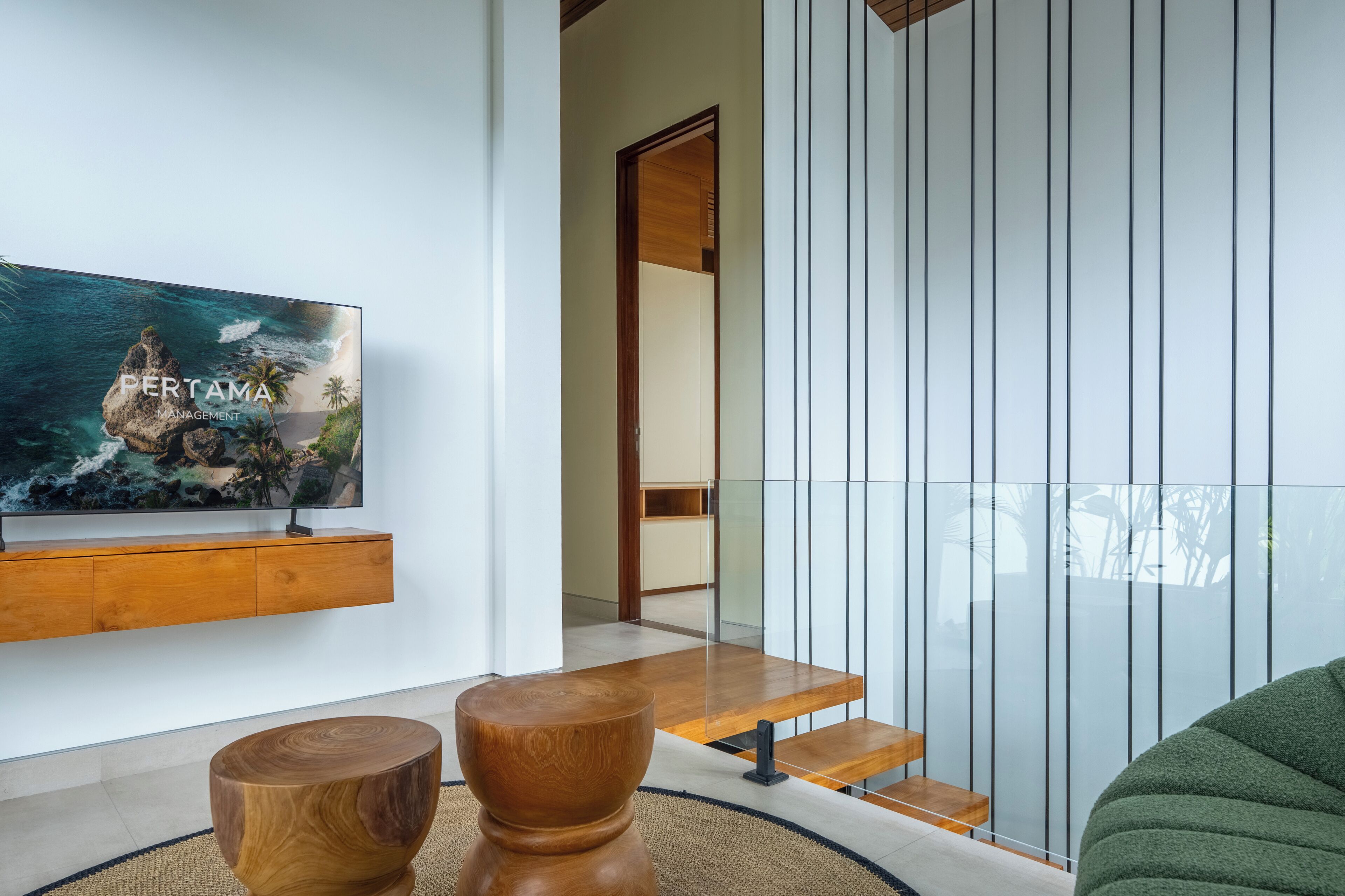 A modern living room with a flat-screen TV, wooden furniture, and a glass partition.