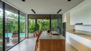 A modern kitchen with a central island, large windows, and a view of a swimming pool. - Villa Rosa by Pertama Stay (Kerobokan)