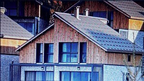 A two-story wooden house with a sloped roof, a garage with a metal gate, and a visible chimney. - Chalet "L'Aster" 6/7pers, breathtaking view, 150m from the slopes, Risoul resort 1850 (RISOUL STATION 1850)