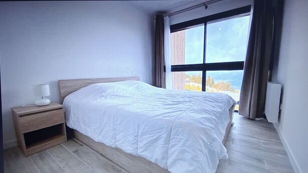 A bedroom with a large bed, a nightstand, a window with curtains, and a view of trees outside. - Chalet "L'Aster" 6/7pers, breathtaking view, 150m from the slopes, Risoul resort 1850 (RISOUL STATION 1850)