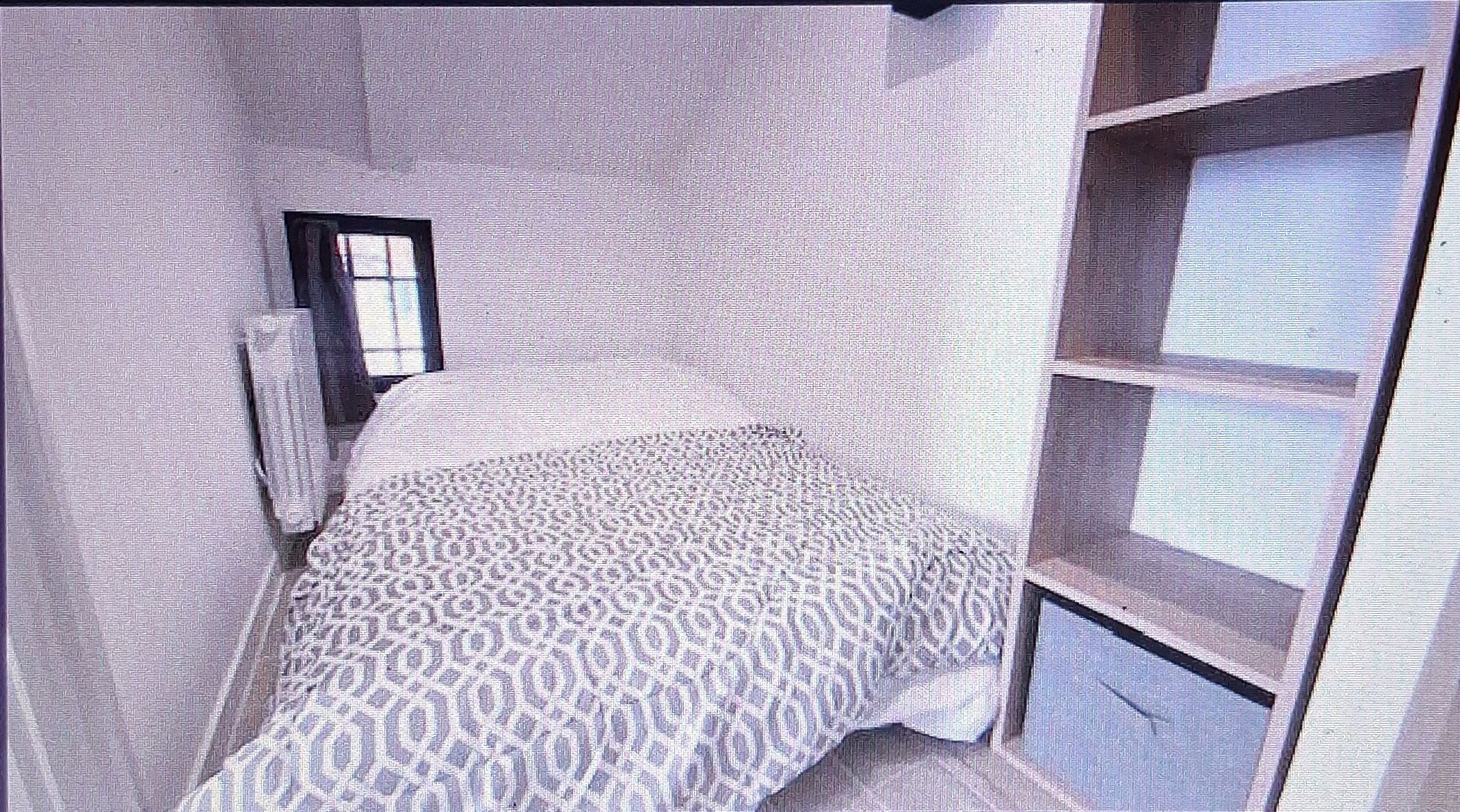 Een slaapkamer met een bed met een decoratieve spreidek, een raam en een ingebouwde wandplank.