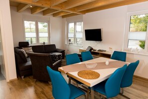 A modern living room with a sofa, chairs, a dining table, and a TV.