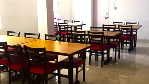 A dining area with multiple tables and chairs, a tiled floor, and a white wall with a no-smoking sign. - HOTEL JADE ARITHANG GANGTOK (Gangtok)